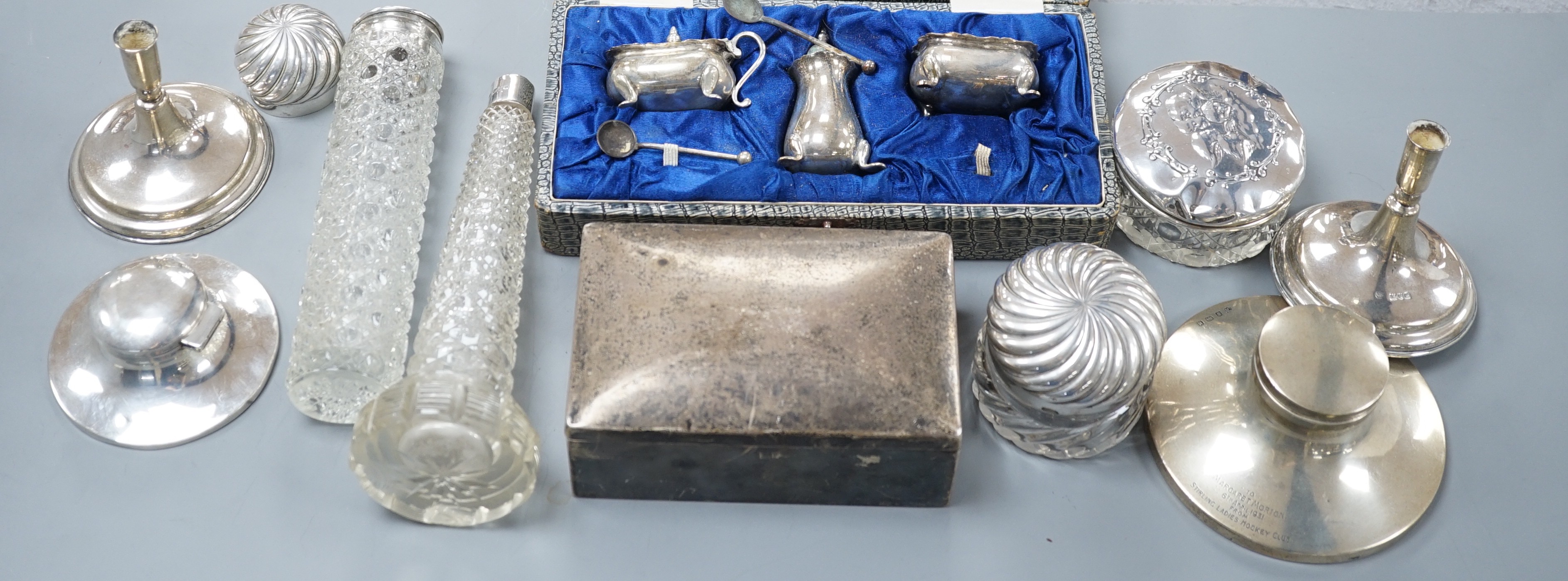 Assorted silver items including a cigarette box, a cased silver condiment set, two capstan inkwells, a pair of Edwardian dwarf candlesticks and four silver mounted glass toilet jars.